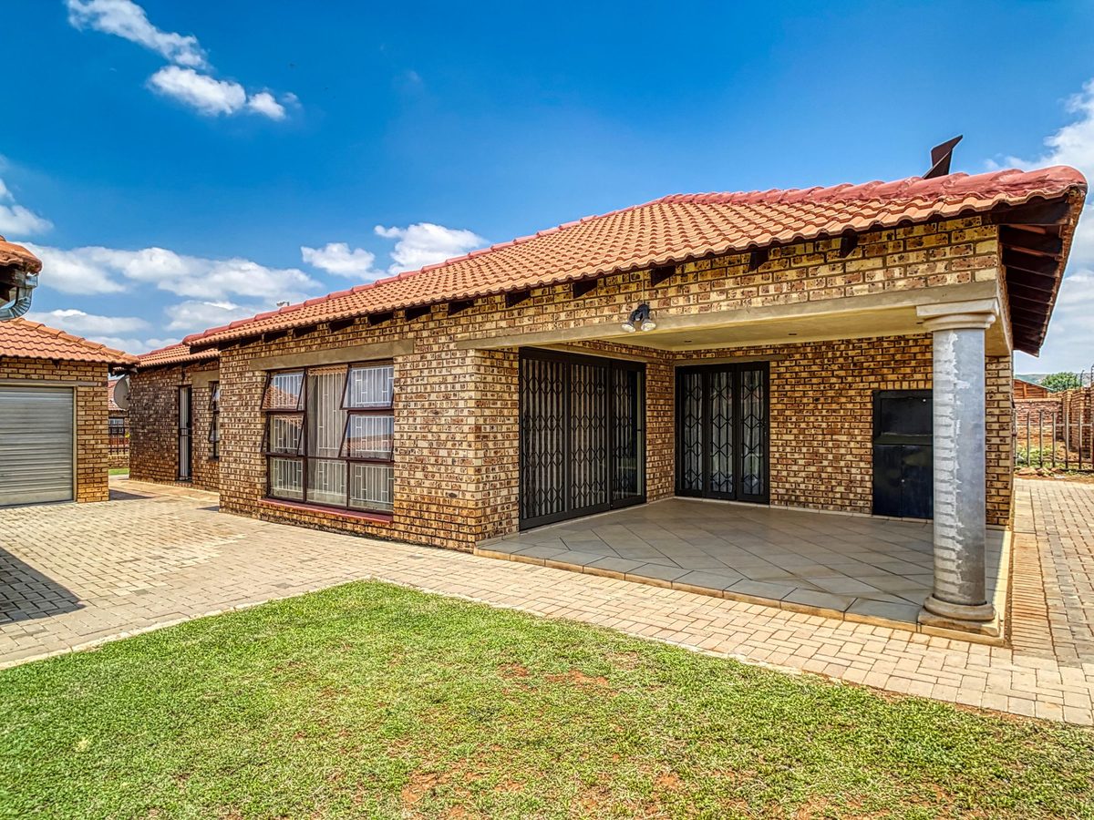 A brick family home with a covered patio and a green lawn.