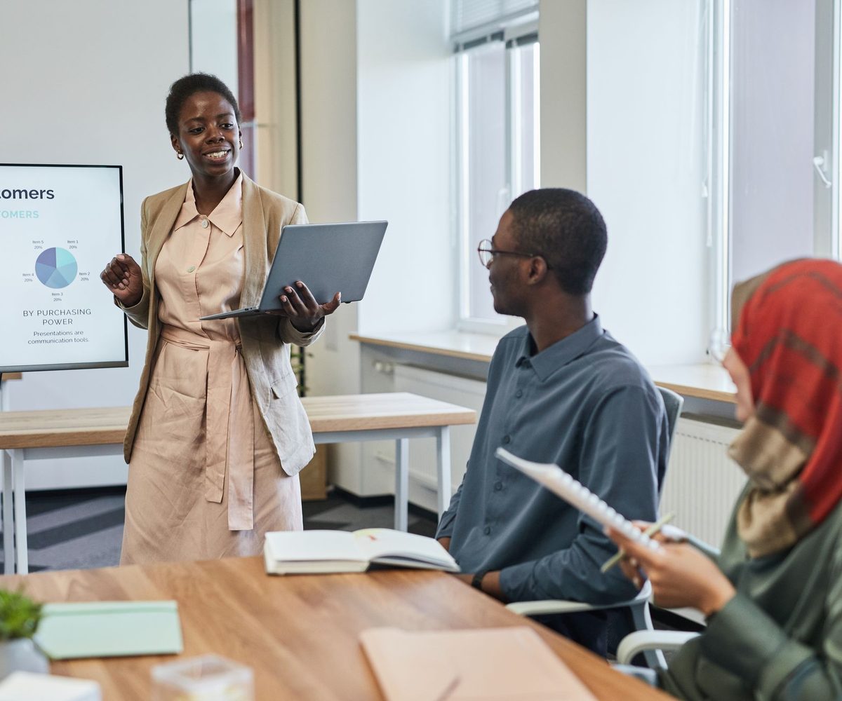 A woman presenting charts on a screen to colleagues seated around a meeting table.