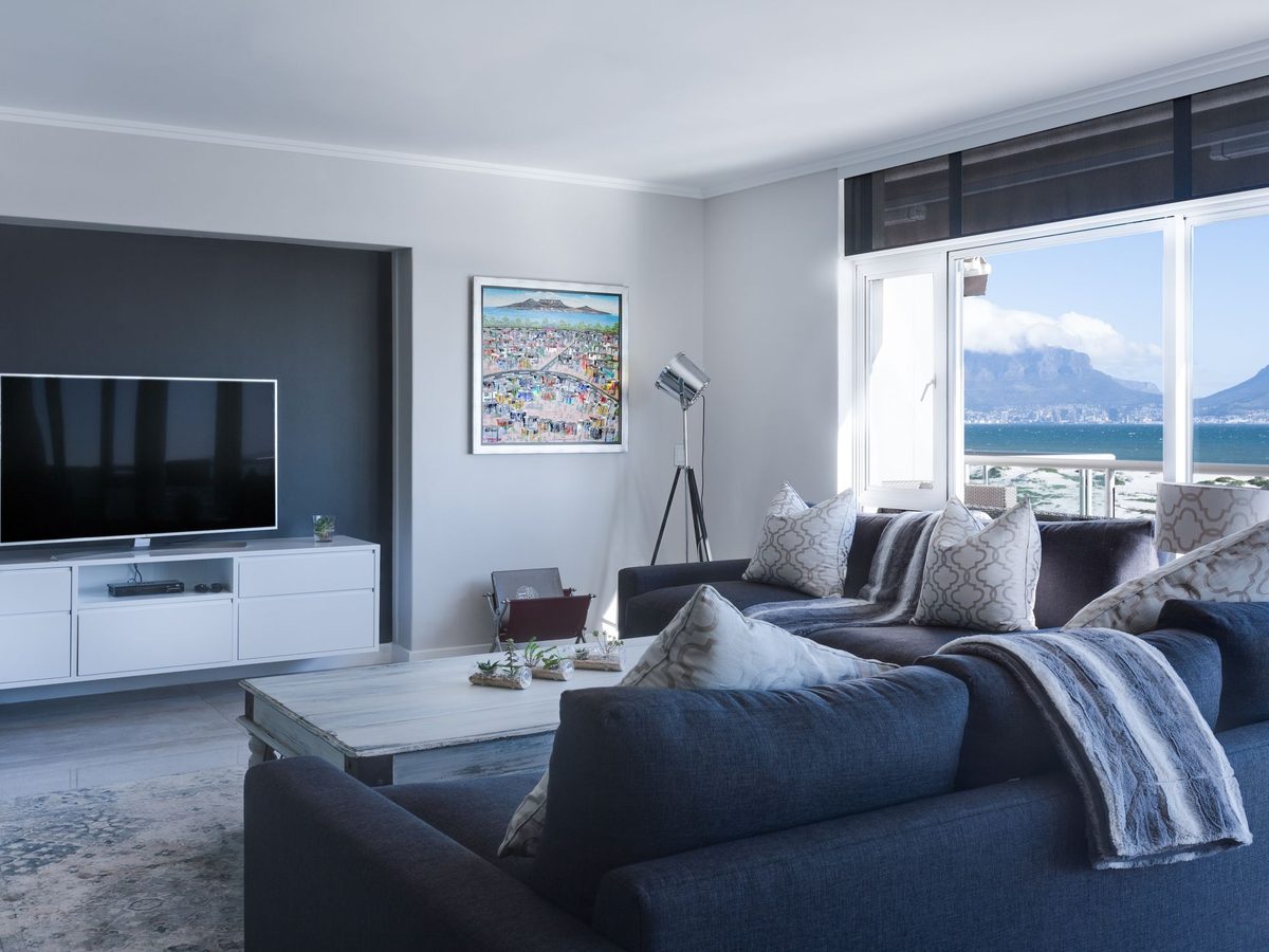 A bright living room with a sea and mountain view through tall windows.