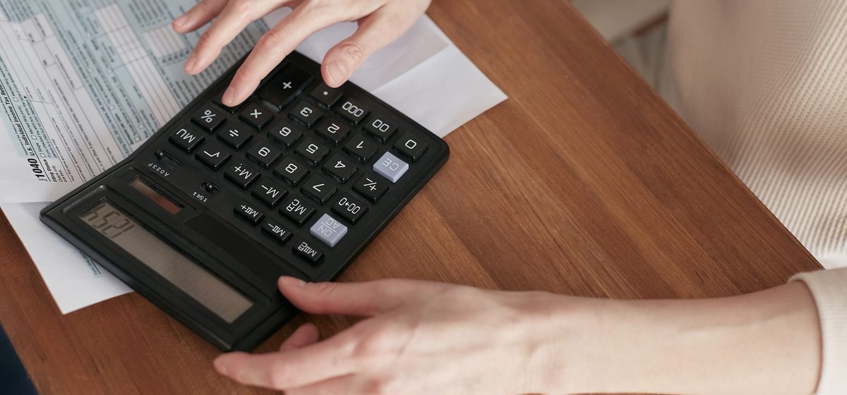 Hands checking a household bill line by line with a calculator.